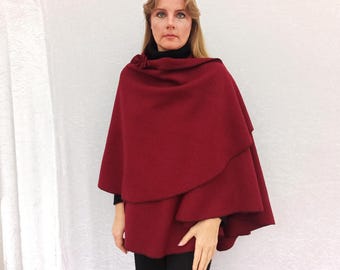 May include: A burgundy wool wrap with a single button closure. The wrap is draped over a person's shoulders and is worn with a black turtleneck.