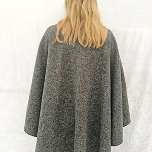 May include: A grey wool cape with a long, flowing design. The cape is being worn by a person with long blonde hair.