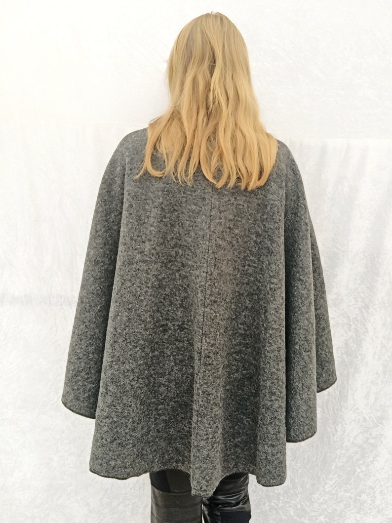May include: A grey wool cape with a long, flowing design. The cape is being worn by a person with long blonde hair.