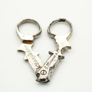 Op de afbeelding: Vintage zilveren champagneflesopener met ringgrepen. De opener heeft een V-vorm, met het woord "Champagne" aan de ene kant en "& Mercier & Co" aan de andere kant gegraveerd. Op een witte achtergrond.