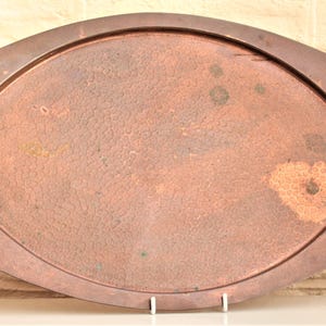 May include: A copper-coloured serving tray with brass handles. The tray has an oval shape with decorative edges and two curved handles. The surface has a textured appearance with some discolouration, suggesting age. The handles are a contrasting brass colour.