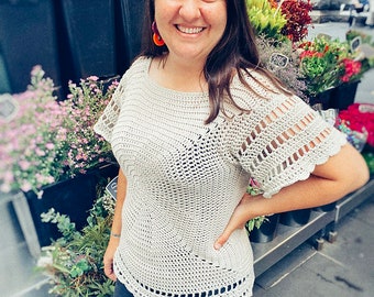 May include: A crocheted top with a light beige color and a scalloped hem. The top has a round neckline and short sleeves with a lacy design.