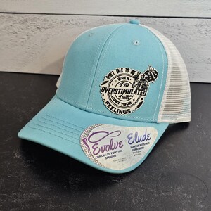 May include: A light blue trucker hat with a white mesh back. The hat features a patch with the text "DON'T TALK TO ME WHEN I'M OVERSTIMULATED I WILL HURT YOUR FEELINGS." The hat also has a concealed ponytail opening.