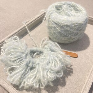 May include: A ball of light blue and white yarn with a crochet hook and a partially crocheted piece of fabric.