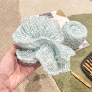 May include: A skein of light blue yarn with a subtle shimmer, perfect for knitting or crocheting. The yarn is soft and fluffy, and it has a delicate texture.