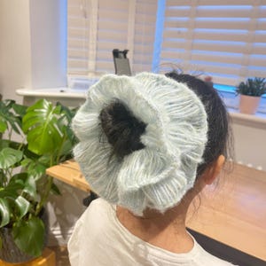 May include: A light blue fluffy scrunchie with a white stripe pattern. The scrunchie is tied around a ponytail.