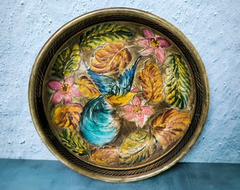 Pode incluir: Uma bandeja redonda de latão com um design floral. A bandeja apresenta um pássaro azul com folhas amarelas, laranja e verdes e flores cor-de-rosa.