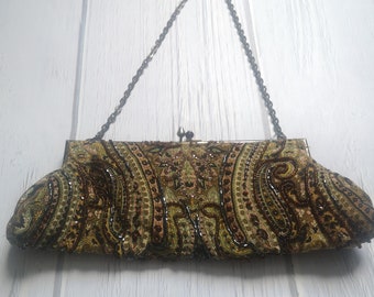 May include: A rectangular clutch bag featuring an intricate paisley pattern in shades of olive green, brown, and cream. The exterior is heavily embellished with dark beads and sequins. It includes a metal frame, a kiss-lock clasp, and a thin chain strap.