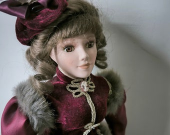 Muñeca de porcelana vintage de los años 60, alta y elegante, con traje victoriano color burdeos. Preciosa muñeca morena de colección, con vestido de terciopelo y detalles de piel. Ideal como regalo para coleccionistas.