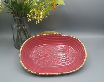 May include: A pink oval ceramic dish with a gold rim and a textured design. The dish is perfect for serving snacks or holding jewelry.
