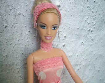May include: A pink and white polka dot dress with a lace trim and a matching headband. The doll has blue eyes and blonde hair.