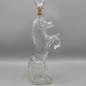 Könnte beinhalten: Transparente Glas-Karaffe in Form eines steigenden Pferdes. Die Flasche hat einen Korken und eine transparente Glaskugel oben. Mähne und Schweif des Pferdes sind detailliert. Die Karaffe ist etwa 30 cm hoch.