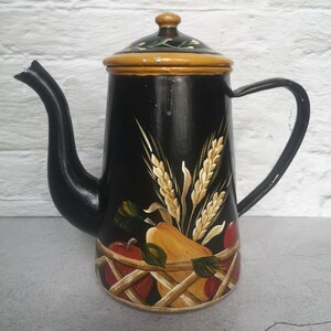 May include: Black metal teapot with a hand-painted design of wheat, apples, and pears in a basket. The teapot has a yellow lid and a black handle.