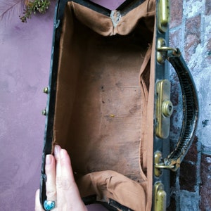 May include: A vintage black leather doctor's bag with brass hardware and a brown fabric lining. The bag is open and empty.
