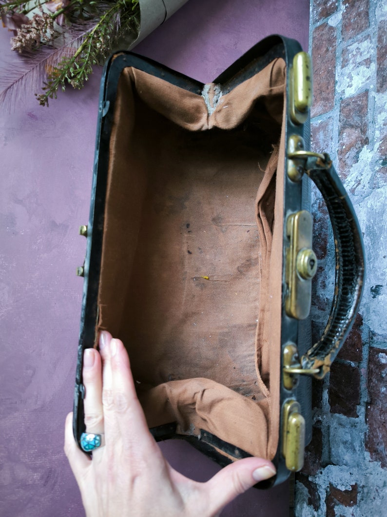 May include: A vintage black leather doctor's bag with brass hardware and a brown fabric lining. The bag is open and empty.