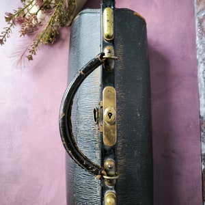 May include: A vintage black leather doctor's bag with brass hardware and a handle. The bag has a worn and aged look, with visible scratches and scuffs.