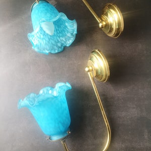 May include: Two wall sconces featuring brass fixtures and turquoise glass shades. The shades are flower-shaped with a speckled pattern. The sconces have a curved arm design and are mounted on round brass bases.