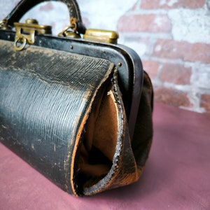 May include: A vintage black leather doctor's bag with brass hardware and a worn, distressed look.
