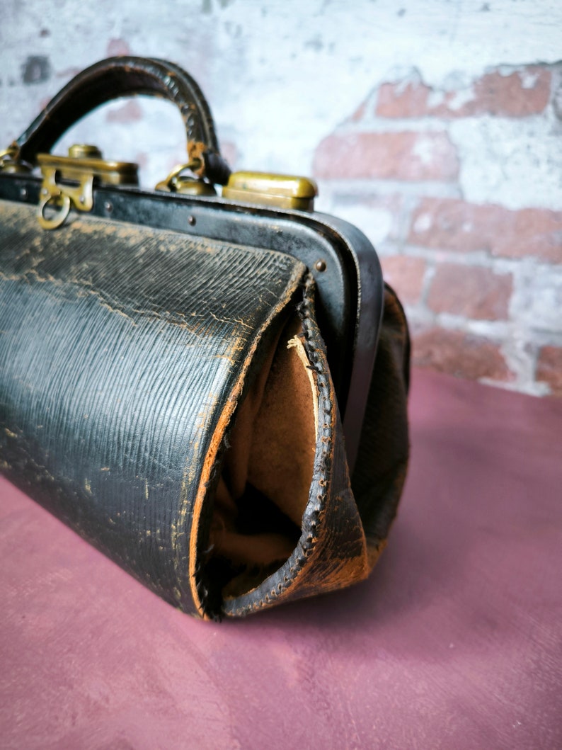 May include: A vintage black leather doctor's bag with brass hardware and a worn, distressed look.
