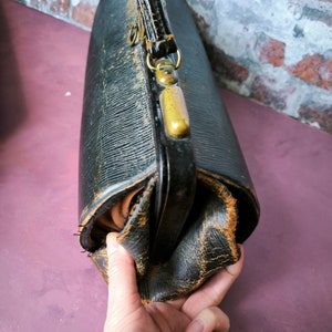 May include: A vintage black leather doctor's bag with brass hardware and a worn, distressed look. The bag has a top handle and a flap closure.