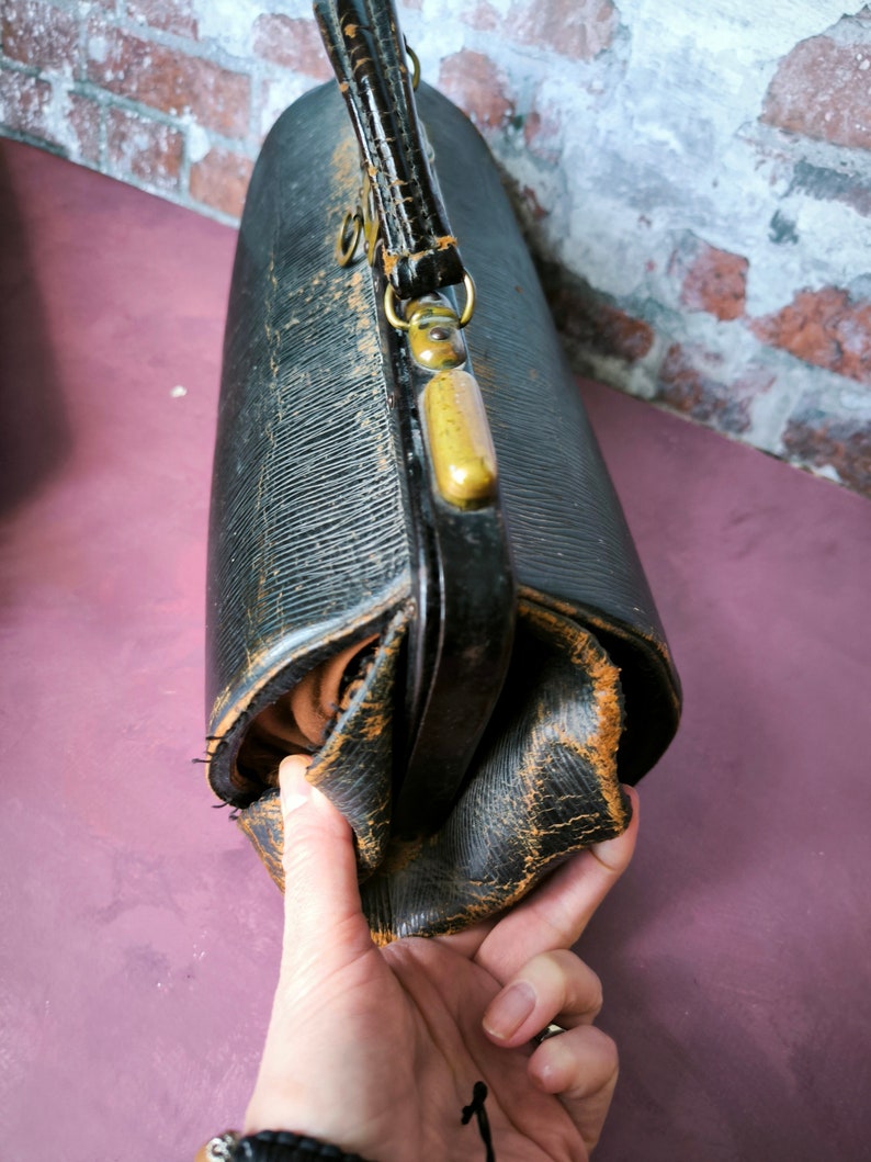 May include: A vintage black leather doctor's bag with brass hardware and a worn, distressed look. The bag has a top handle and a flap closure.