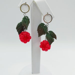 May include: A pair of dangle earrings featuring red raspberry-shaped charms with green leaf accents. The earrings are made with silver-toned metal.