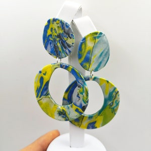 May include: A pair of yellow, blue, and white marbled circle earrings. The earrings are on a white display stand.
