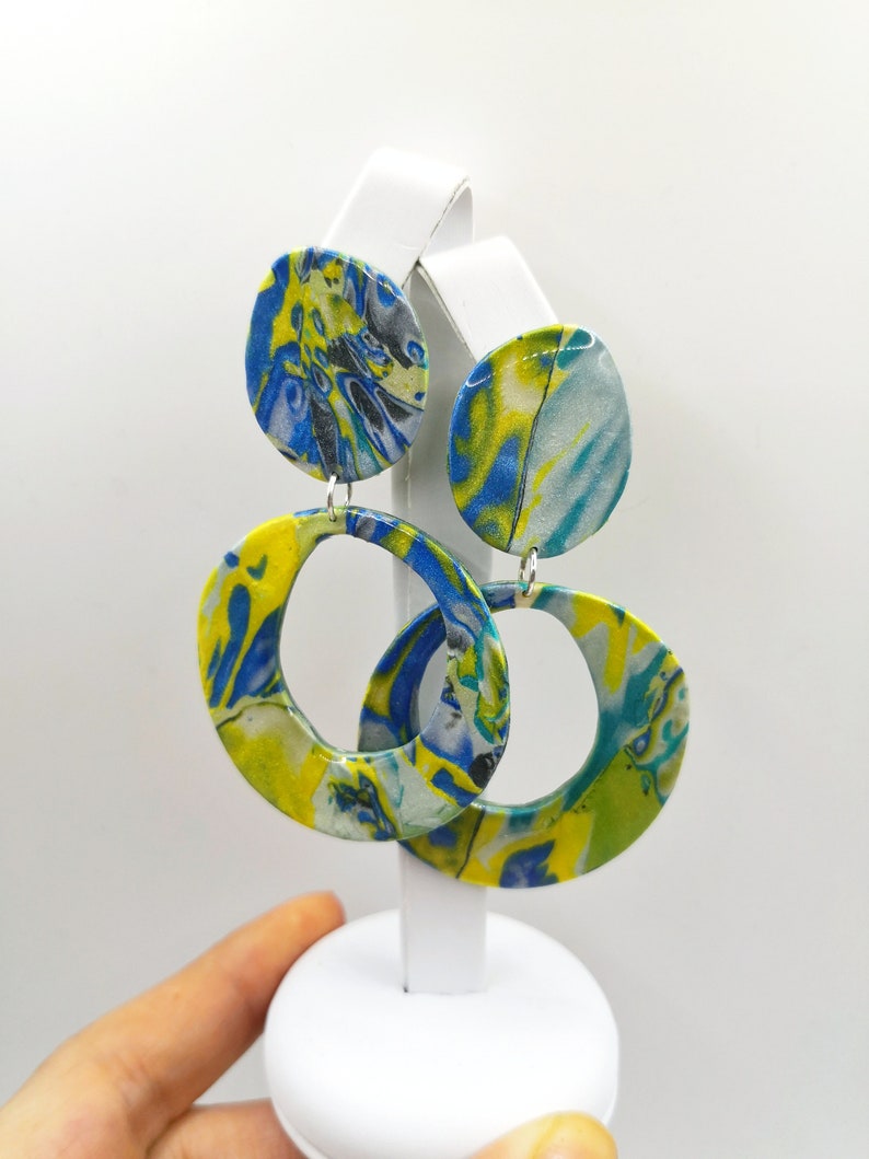 May include: A pair of yellow, blue, and white marbled circle earrings. The earrings are on a white display stand.
