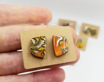 Puede incluir: Un par de pendientes de cerámica con forma geométrica. Un pendiente es naranja y amarillo con detalles negros, el otro es amarillo y negro con detalles blancos.