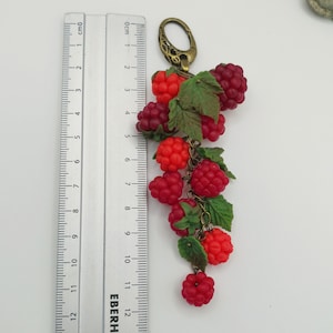 May include: A charm bracelet with a gold-toned chain and a cluster of red and green polymer clay raspberries. The charm is approximately 13 cm long.