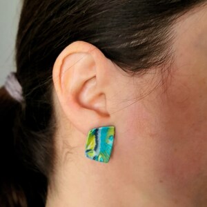 May include: A pair of green, blue and white patterned earrings. The earrings are shaped like a rectangle with rounded corners.