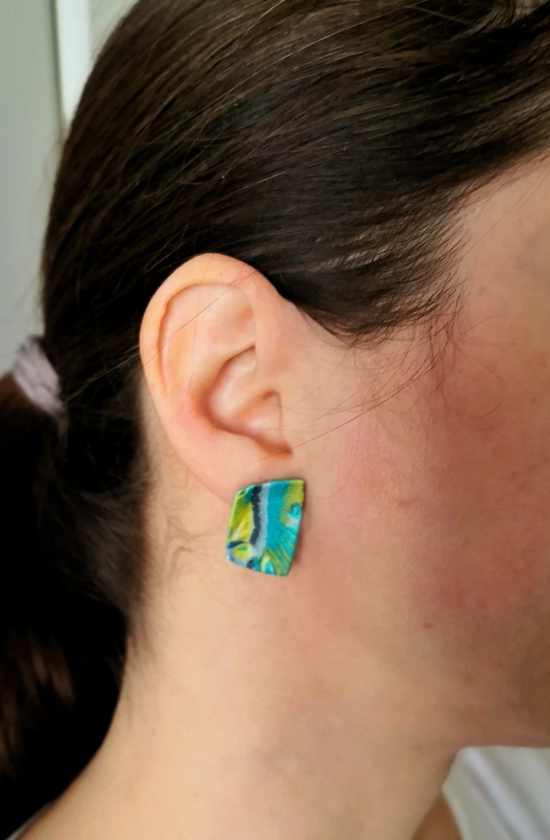 May include: A pair of green, blue and white patterned earrings. The earrings are shaped like a rectangle with rounded corners.