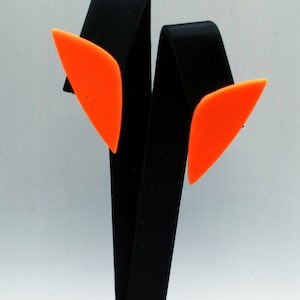 May include: A pair of orange geometric shaped earrings on a black display stand.