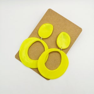 May include: A pair of neon yellow dangle earrings with a large oval shape and a smaller oval shape on top. The earrings are on a brown card.