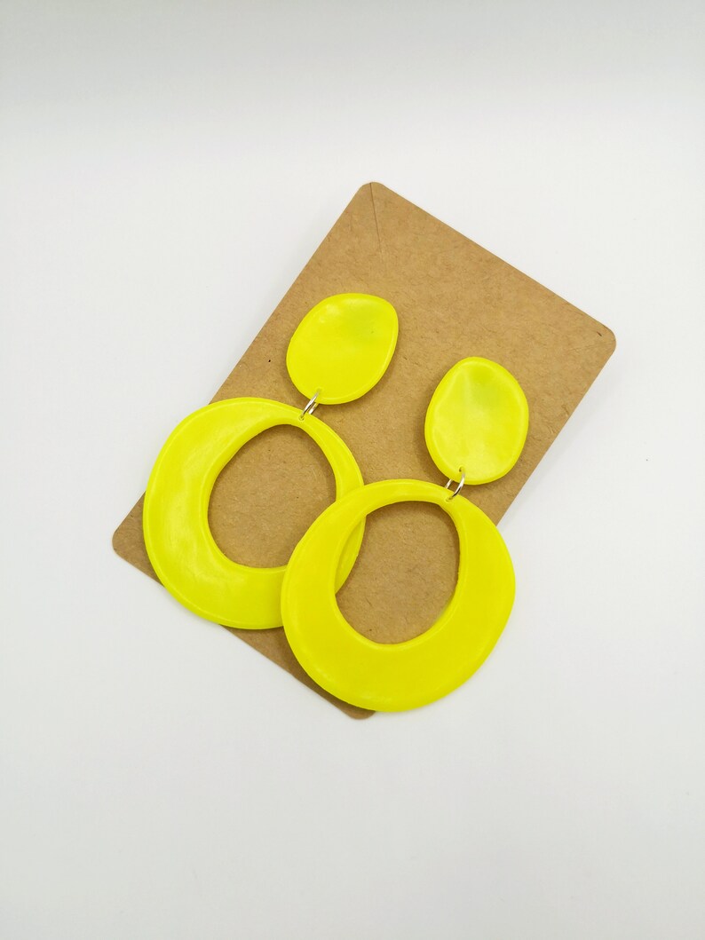 May include: A pair of neon yellow dangle earrings with a large oval shape and a smaller oval shape on top. The earrings are on a brown card.