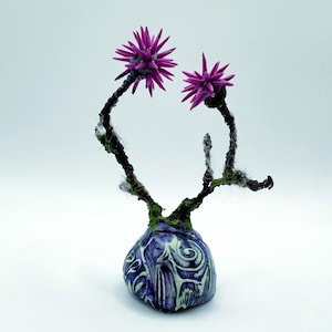Könnte beinhalten: Eine kleine Keramikvase mit einem blauen und weißen Wirbelmuster, die eine handgefertigte Drahtskulptur mit zwei rosa Blüten hält.