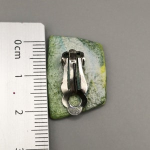 May include: A pair of green, blue and white clip-on earrings with a silver metal clasp.