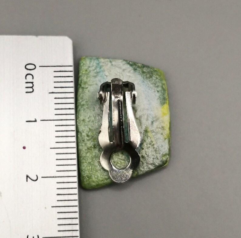 May include: A pair of green, blue and white clip-on earrings with a silver metal clasp.