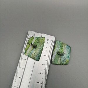May include: A pair of green and white rectangular earrings with silver clasps. The earrings are approximately 2 cm in length.