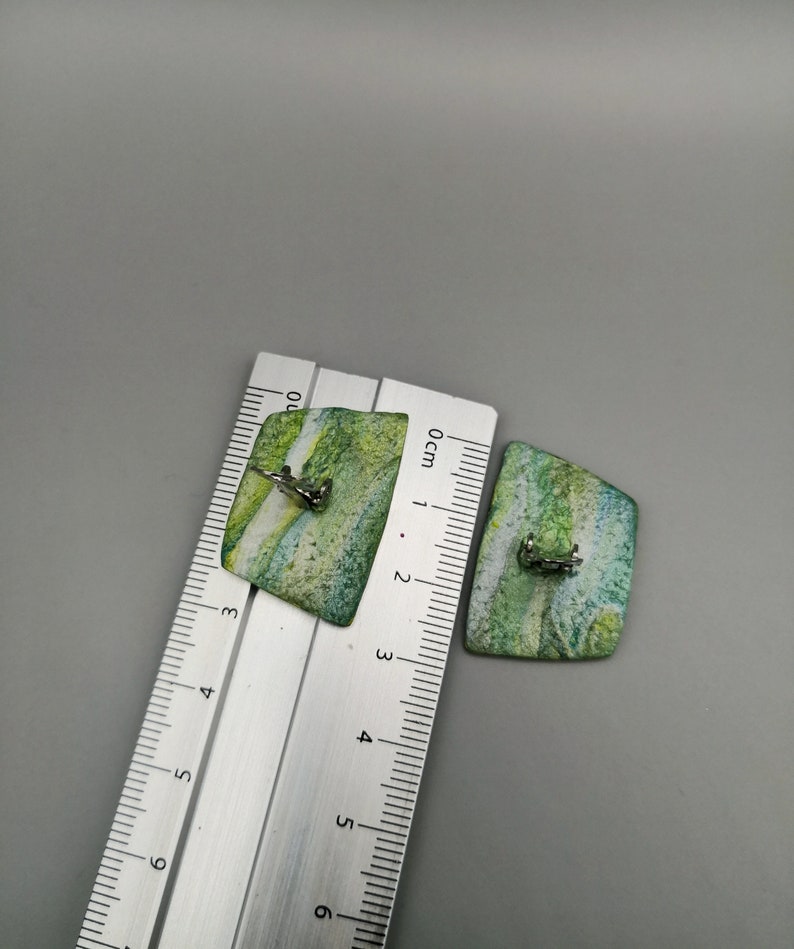May include: A pair of green and white rectangular earrings with silver clasps. The earrings are approximately 2 cm in length.