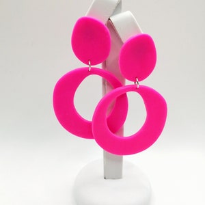 May include: A pair of pink statement earrings with a large circle and a smaller round shape. The earrings are made of a smooth, matte material.