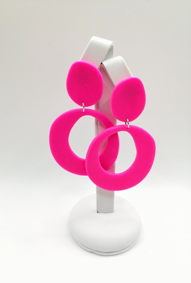 May include: A pair of pink statement earrings with a large circle and a smaller round shape. The earrings are made of a smooth, matte material.