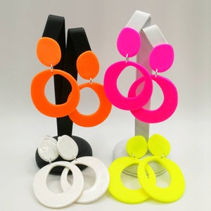May include: Three pairs of neon colored earrings. The earrings are made of plastic and have a large circle design. The colors are orange, pink, and yellow.