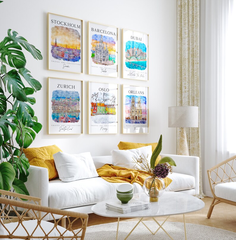 May include: Six watercolor cityscapes in gold frames, featuring scenes from Stockholm, Barcelona, Dubai, Zurich, Oslo, and Orleans. The prints are displayed on a white wall in a living room setting.