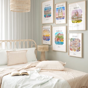 May include: A bedroom interior with a white bed, a wooden nightstand with a lamp, and six framed watercolor paintings of cityscapes. The paintings feature cities such as Zurich, Orleans, Seoul, Stockholm, Norway, and Italy.