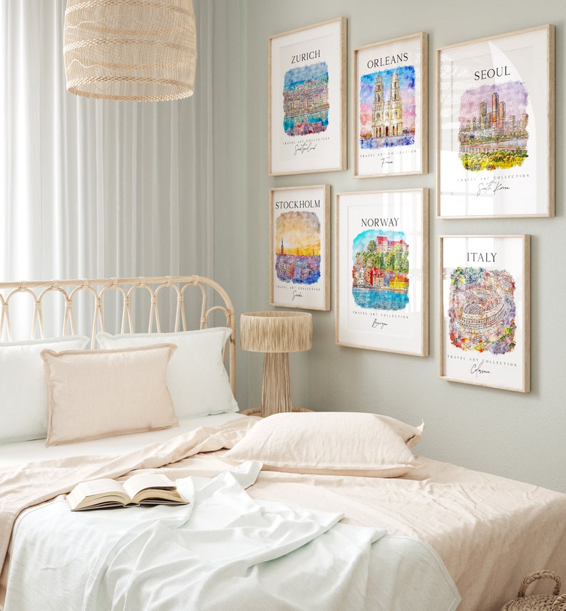 May include: A bedroom interior with a white bed, a wooden nightstand with a lamp, and six framed watercolor paintings of cityscapes. The paintings feature cities such as Zurich, Orleans, Seoul, Stockholm, Norway, and Italy.