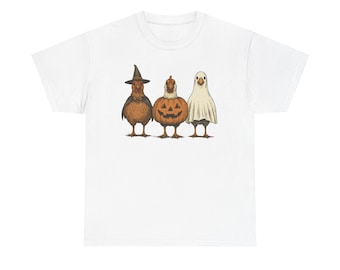 Peut inclure: T-shirt blanc avec une illustration d'Halloween de trois poulets. L'un est déguisé en sorcière, un autre en citrouille et le troisième en fantôme. Le design a une esthétique vintage dessinée à la main.