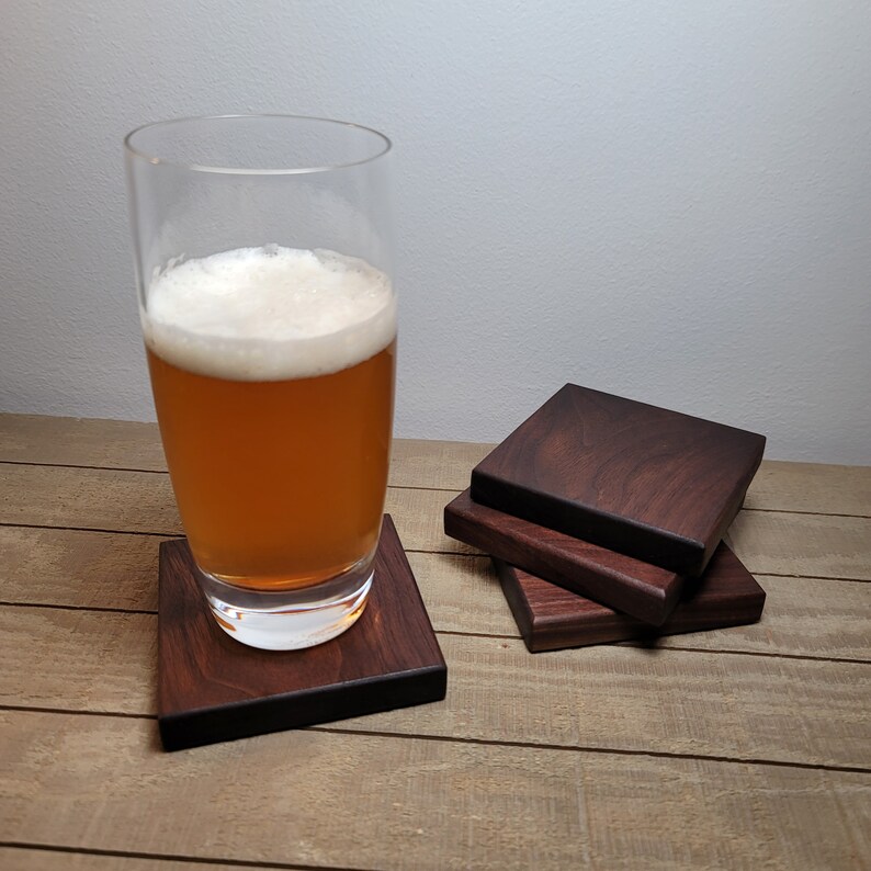 May include: A glass of beer on a dark brown wooden coaster. Four coasters are stacked next to the glass.