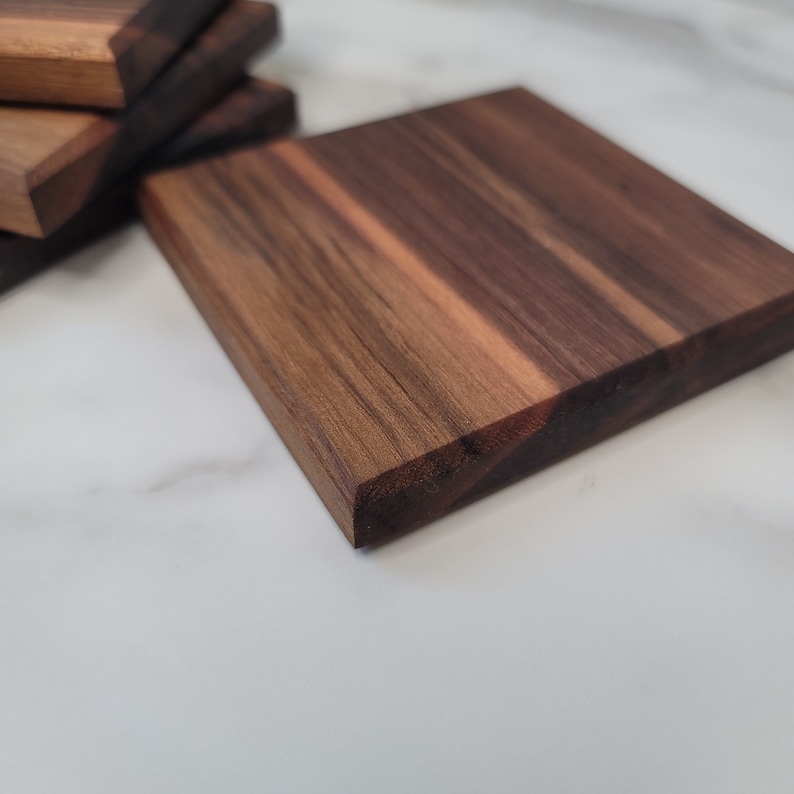 May include: A close-up of a square wooden coaster with a dark brown wood grain. The coaster has a smooth, polished surface.