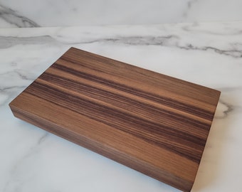 May include: A rectangular wooden cutting board with a rich brown and dark brown striped pattern. The board has a smooth surface and a thick, sturdy design, perfect for kitchen use.